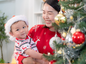 A baby with his mom beside a decorated Christmas tree, celebrating together at home during the Christmas season.