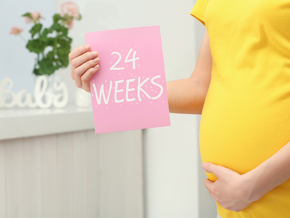 A cropped photo of 24 weeks pregnant Asian woman holding a card with the text 24 WEEKS near her belly