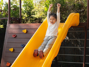 A happy child sliding down a playground slide outdoors, representing active play, childhood joy,  and the importance of supporting kids’ immune and respiratory health