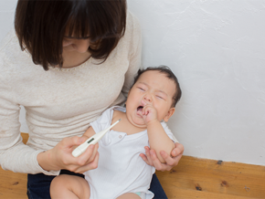 A mother checks a thermometer while carrying her baby on her lap, wondering if he has a teething fever