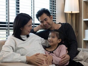 A pregnant woman and her husband with their stepdaughter on a couch, happy as a blended family.