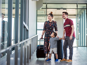 A young Asian mom, dad, and little boy at the airport with suitcases, getting ready to create memories through family travel.