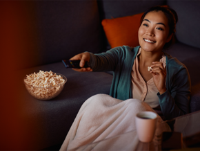 A young Asian mom relaxing on the sofa with a bowl of snacks, watching mom movies