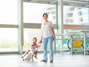 A young Asian mom with her young toddler riding on her luggage at the airport.