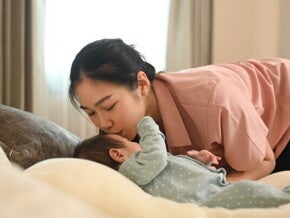 A young Asian mother kisses her baby goodbye, experiencing separation anxiety as she leaves for work.