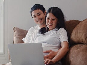 A young Asian pregnant couple with a laptop at home, applying online for the expanded maternity leave