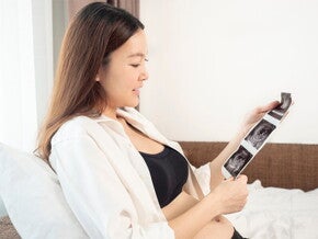 A young Asian woman in bed looking at her ultrasound at 13 weeks pregnant