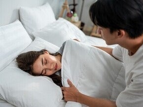 An Asian man puts a blanket on his wife with a headache and lets her rest, helping her through early pregnancy pain areas