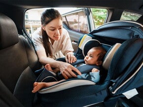 An Asian woman fastening her infant into a rear-facing car seat.