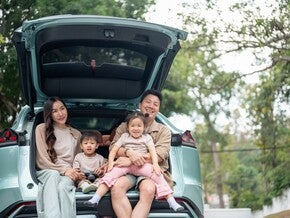 A happy Asian family sitting in the trunk of their car, enjoying a pit stop on their road trip.