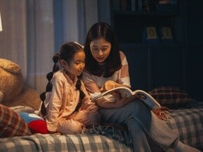 Asian mom and daughter reading a book at night as a daily routine.