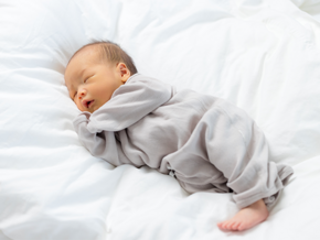 Asian newborn grunting while sleeping on white sheets.