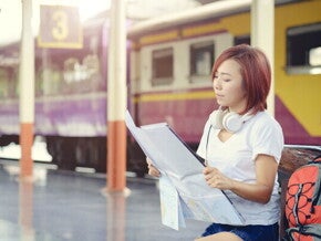 Asian woman reading a map in front of a train. 