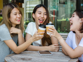 Happy Asian women friends sitting in a cafe, drinking coffee and talking together as a support system.