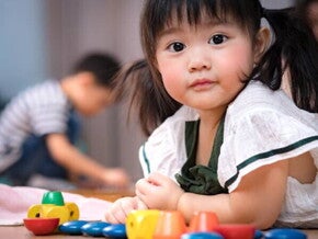 Asian 2-year-baby girl lies on her stomach on the floor while playing with her toys.