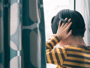 Asian child with special needs covers his ears as he faces the window