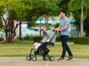 Asian dad pushes his baby's stroller through a park