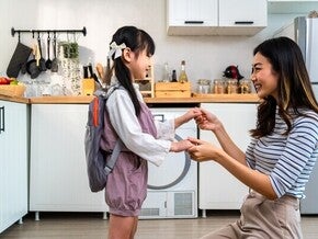 Asian mom holding little girl’s hand in the kitchen after giving her baon bag with milk products for school
