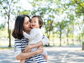 Asian mom kisses her toddler while carrying her in her arms during a walk in a park