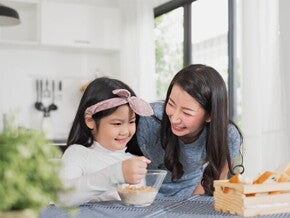 Asian mother watching her child eating cereal from a bowl