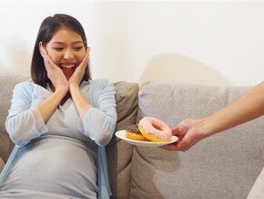 Asian pregnant woman reacts with a big smile as she's offered donuts on a plate. Asian pregnant woman reacts with a big smile as she's offered donuts on a plate.