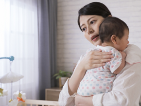 Asian young woman burps her baby over her shoulder after feeding. 