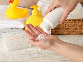 Close-up pic of one hand pouring baby powder onto the other hand, with towels and a yellow rubber duck in the background.