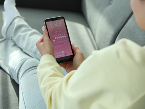 Close-up photo of a woman seated on the couch and using a period calculator on her phone.