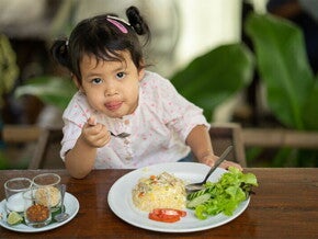 Cute Asian little girl eats fried rice with tomatoes and green leafy vegetables on the side