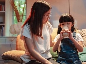 Asian mom watching her little girl drinking milk before bed, wondering does milk help you sleep?