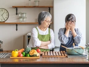 Elderly Asian woman berating a younger woman to tears in the kitchen.