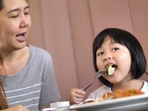 Filipino mother with daughter eating together at home for healthy weight gain.
