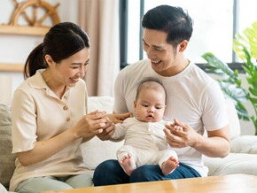 Filipino mom smiles at her newborn who's being held by her husband on his lap.
