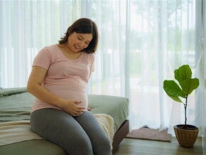 Happy pregnant Asian woman touches her pregnant belly while sitting on the bed. Happy pregnant Asian woman touches her pregnant belly while sitting on the bed.