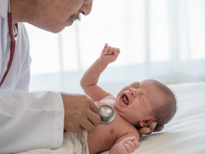 Photo of a doctor examining a newborn in the hospital with a stethoscope.