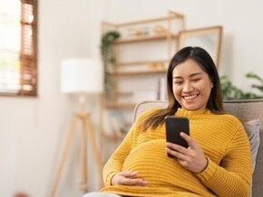 Pregnant Asian woman using her phone to message her ob-gyne for her birth plan.