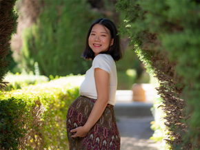 Smiling pregnant Asian woman wearing a cotton dress outdoors and showing off her baby bump.