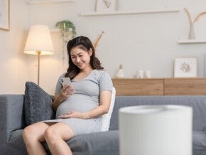 Pregnant Asian woman on a sofa looking at her pregnancy app on her phone at home