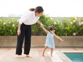 Asian mom holding preschooler daughter’s hand by the edge of the pool, teaching her water safety rules. 