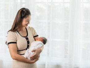 A new mom holding her newborn baby while standing at home, happy with her self-care plan.