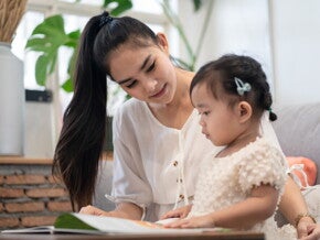 A young Asian mother and her daughter reading a Filipino children’s book together. 