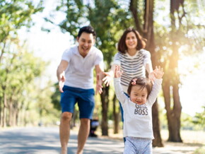 Cute Asian toddler wearing a “girl boss” shirt lifts her arms as her parents reach out to her in the background. Cute Asian toddler wearing a “girl boss” shirt lifts her arms as her parents reach out to her in the background.