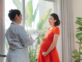 Happy Asian pregnant woman in red talking to doctor. Happy Asian pregnant woman in red talking to doctor.