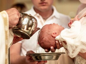 Catholic priest pours water over a baby's head for a christening or baptism ceremony.