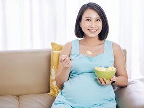 Teaser_Image Young and smiling Asian pregnant woman eat a bowl of fruits good for pregnancy.