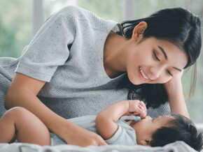 Young Filipino mom smiles down at her baby as she lies down beside them.