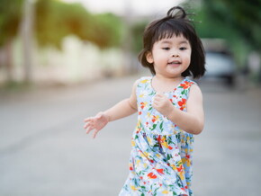 Asian female toddler runs in the street during summertime.