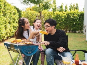 Asian family enjoying barbecued corn outdoors.