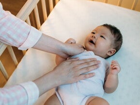 Baby Sleeping Position Basics Asian baby being put to sleep on their back in safe crib.