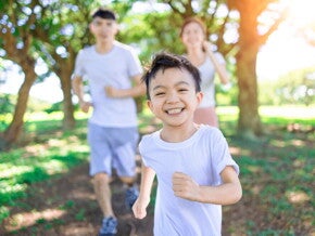 Teaser_Image Happy healthy Asian boy running in the park with his parents behind him